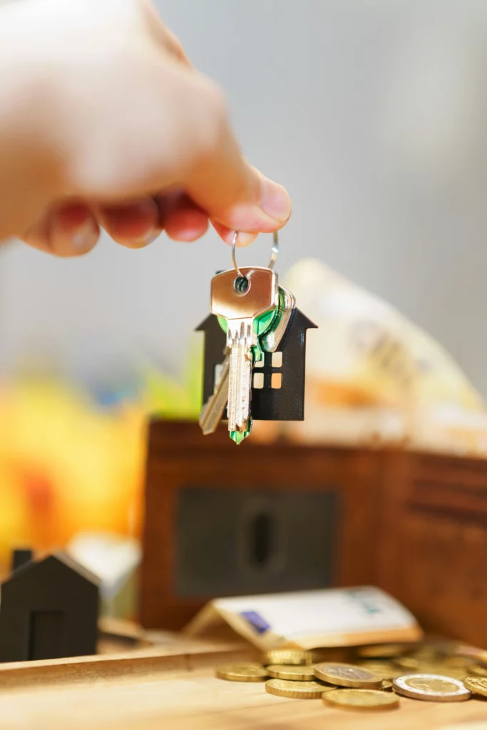 Keys and small house held above a miniature house and some cash.